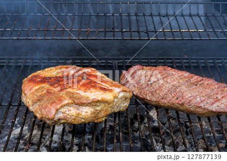 Juicy cuts of meat sizzle on grill, releasing mouthwatering aromas as they cook during an outdoor barbecue. Juicy cuts of meat sizzle on grill, releasing mouthwatering aromas as they cook during an outdoor barbecue. 127877139