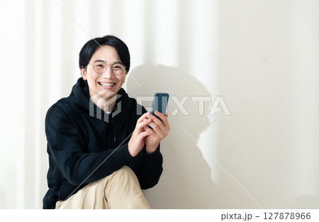 壁際でスマホを見る男性 127878966