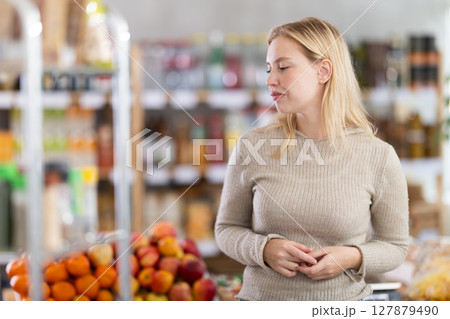 Portrait of girl shopper with a shopping cart choosing some products in supermarket Portrait of girl shopper with a shopping cart choosing some products in supermarket 127879490