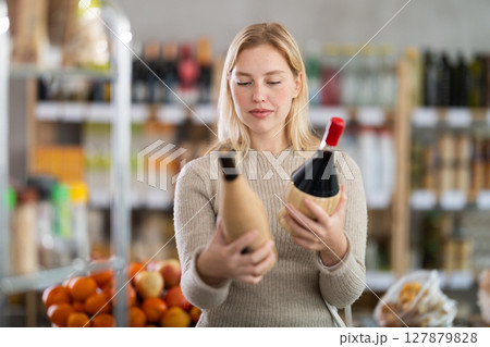 Shopping in produce supermarket - female buyer makes choice bottle of wine Shopping in produce supermarket - female buyer makes choice bottle of wine 127879828