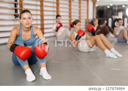 Girls in boxing gloves are sitting on floor, doing abdominal exercise and working with hands Girls in boxing gloves are sitting on floor, doing abdominal exercise and working with hands 127879864