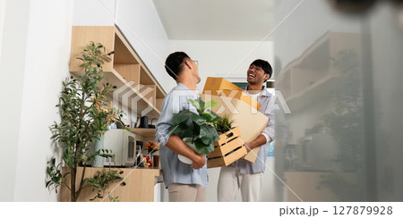 Joyful gay couple unpacking boxes and plants in their new apartment Joyful gay couple unpacking boxes and plants in their new apartment 127879928