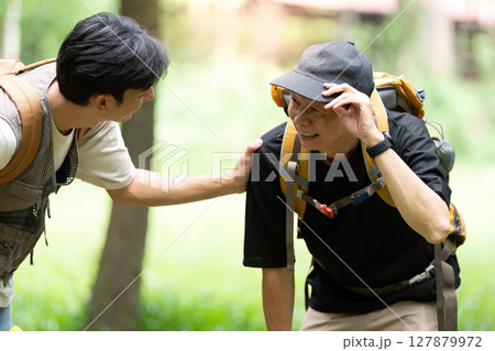 Father Supporting Son During Hike. A father comforting his son while taking a break in the woods. Father Supporting Son During Hike. A father comforting his son while taking a break in the woods. 127879972
