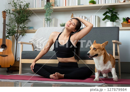 Stretching and Wellness. Woman enjoying yoga stretches with her dog in a cozy living room. 127879984