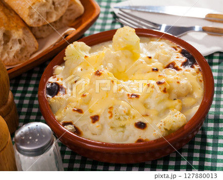 Tasty baked cauliflower with bechamel sauce in clay pot at table 127880013