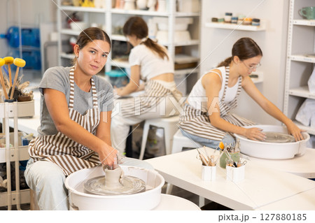 Three young women sits near potter wheel and makes clay crafts 127880185