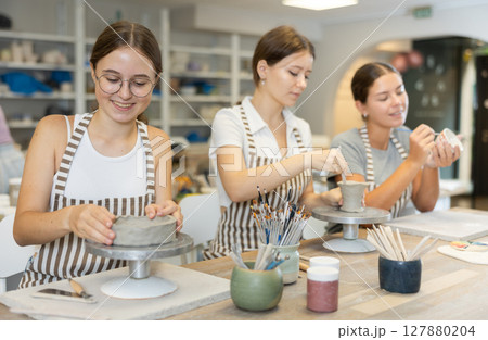 Three craftsperson are busy sculpting from clay and painting ceramic products 127880204