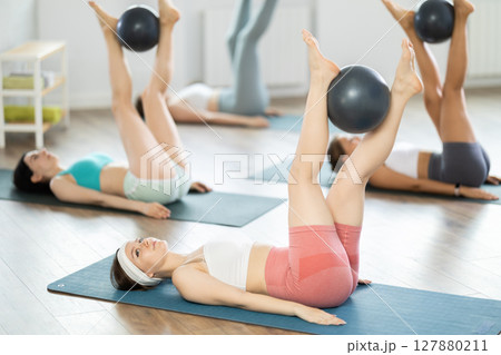 Lying on their backs, young girls hold Pilates ball between their knees and perform leg exercises Lying on their backs, young girls hold Pilates ball between their knees and perform leg exercises 127880211