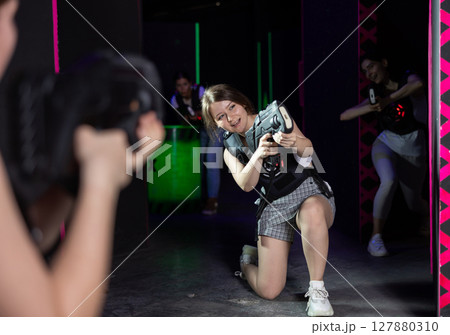 Joyous girl with laser pistol playing laser tag with girlfriends on labyrinth Joyous girl with laser pistol playing laser tag with girlfriends on labyrinth 127880310