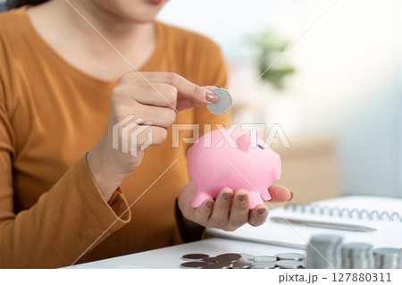 Savings and Financial Planning. Individual adding coins to pink piggy bank. 127880311