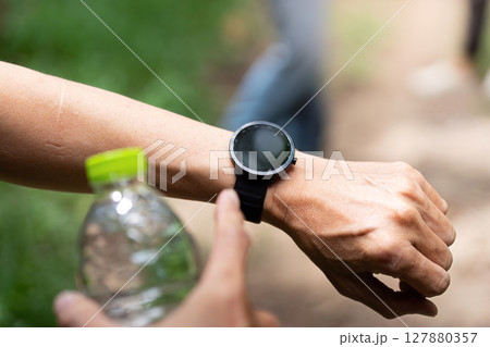 Close-Up of Smartwatch and Water Bottle. A detailed view of a smartwatch and water bottle during a hiking trip. 127880357