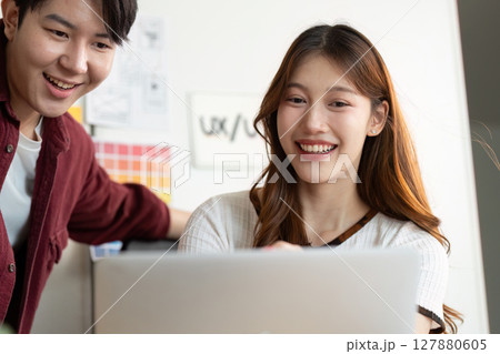 Engaged Teamwork. Young professionals smiling while reviewing design work on laptop. 127880605