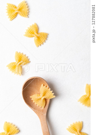Flat lay of raw farfalle pasta on a wooden spoon placed on a white background, Bow-tie shaped pasta 127882081