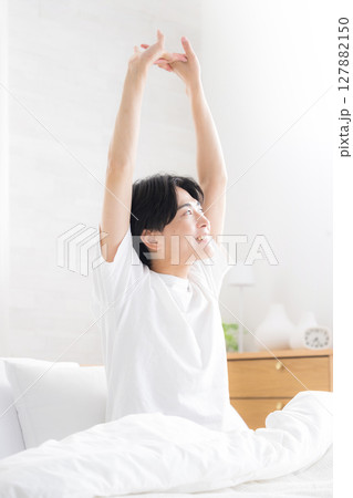 朝日を浴びるベッドで寝起きの若い男性　腕を伸ばしストレッチをするクローズアップ 127882150