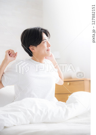 朝日を浴びるベッドで寝起きの若い男性 腕を伸ばしストレッチをするクローズアップ 朝日を浴びるベッドで寝起きの若い男性 腕を伸ばしストレッチをするクローズアップ 127882151