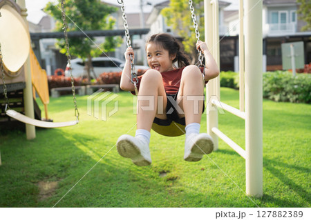 Happy child playing on swing in sunny playground with green grass and cheerful atmosphere, enjoying carefree moments of childhood laughter and joy Happy child playing on swing in sunny playground with green grass and cheerful atmosphere, enjoying carefree moments of childhood laughter and joy 127882389