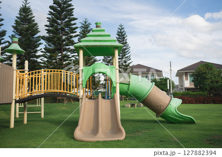 Colorful playground structure with slide and climbing area in a grassy park setting under a bright sky with trees in the background Colorful playground structure with slide and climbing area in a grassy park setting under a bright sky with trees in the background 127882394