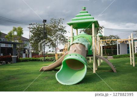 Vibrant Play Area with Green Slide and Tower in Outdoor Park Surrounded by Grass and Trees Under a Cloudy Sky Vibrant Play Area with Green Slide and Tower in Outdoor Park Surrounded by Grass and Trees Under a Cloudy Sky 127882395