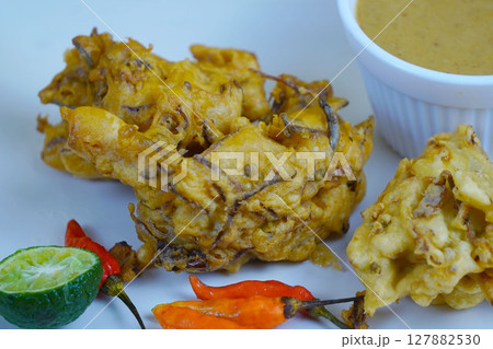 A plate of Bakwan or golden-brown Indonesian fritters served with a dipping sauce, lime, and chili peppers. 127882530