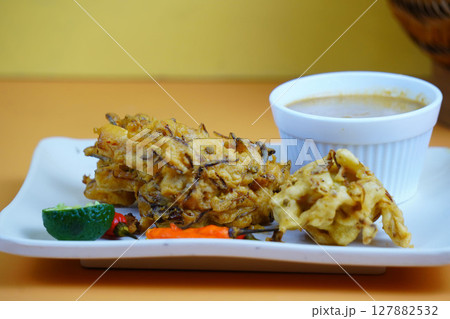 A plate of Bakwan or golden-brown Indonesian fritters served with a dipping sauce, lime, and chili peppers. A plate of Bakwan or golden-brown Indonesian fritters served with a dipping sauce, lime, and chili peppers. 127882532