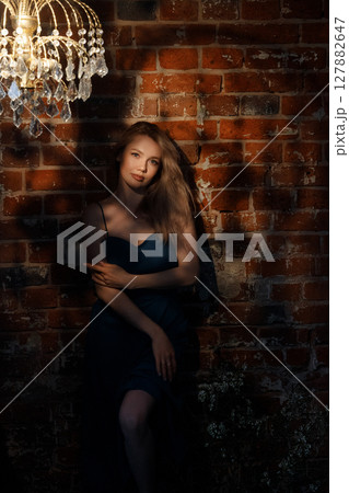 Woman in blue dress standing in shadow near vintage brick wall and crystal chandelier 127882647
