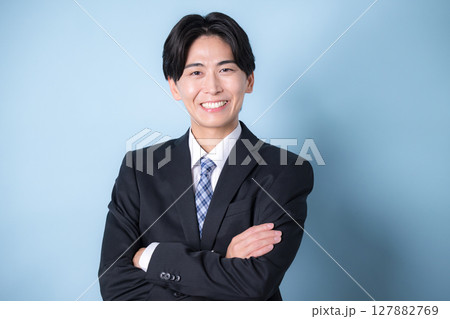 カメラ目線でスーツを着たビジネスマンの腕組みの若い男性水色　爽やかなイメージ 127882769