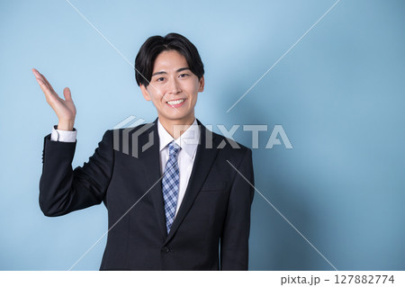 カメラ目線でスーツを着たビジネスマンの若い男性水色背景　笑顔の爽やかなイメージ　オススメや案内 127882774