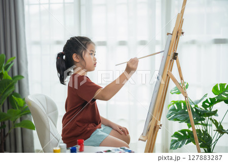 Child Artist Creating Masterpiece on Canvas with Paintbrush in Cozy Indoor Space Filled with Natural Light and Indoor Plants 127883287