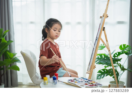 Young girl painting on canvas in bright room with natural light, showcasing creativity and artistic talent using brushes and vibrant colors 127883289