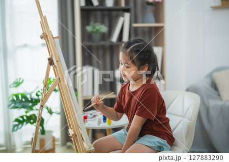 Young girl artist painting on easel in bright room filled with plants and natural light, showcasing creativity and passion for art expression Young girl artist painting on easel in bright room filled with plants and natural light, showcasing creativity and passion for art expression 127883290
