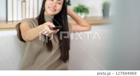 Cheerful woman pointing remote control. Enjoying TV time at home. 127884069