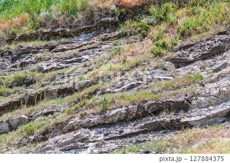 Rock of layered stone overgrown with grass and moss. 127884375