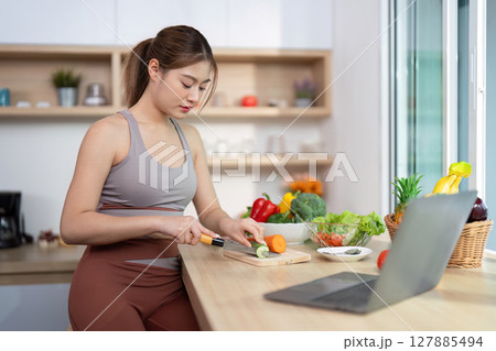 Wellness and Meal Preparation. Young woman chopping vegetables in a bright kitchen. Wellness and Meal Preparation. Young woman chopping vegetables in a bright kitchen. 127885494