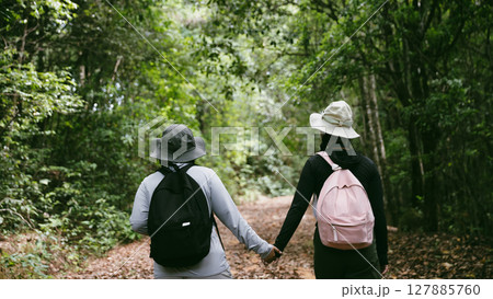 Two female friends with backpacks on vacation hiking through countryside together. Asian friend girls backpacker friend travel in forest wild together. happy and enjoying sunny day while hiking. 127885760