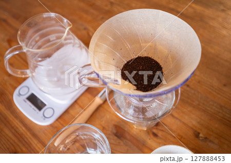 【日本】木目のテーブル上に置かれた計りとコーヒーサーバーと挽いたコーヒー豆を入れたフィルター 【日本】木目のテーブル上に置かれた計りとコーヒーサーバーと挽いたコーヒー豆を入れたフィルター 127888453