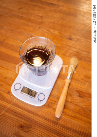 【日本】木目のテーブル上の計りにコーヒーが入ったグラスを置いて重さを測っているところ 【日本】木目のテーブル上の計りにコーヒーが入ったグラスを置いて重さを測っているところ 127888464