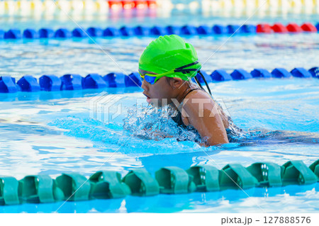 Swimmer child swims breaststroke swimming style in a race swimming pool. Water sports and competition, learning to swim classes for children. 127888576