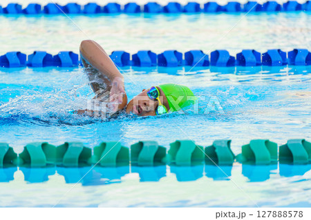 Swimmer child swims freestyle swimming style in a race swimming pool. Water sports and competition, learning to swim classes for children. Swimmer child swims freestyle swimming style in a race swimming pool. Water sports and competition, learning to swim classes for children. 127888578