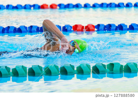 Swimmer child swims freestyle swimming style in a race swimming pool. Water sports and competition, learning to swim classes for children. 127888580