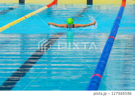Swimmer child swims butterfly swimming style in a race swimming pool. Water sports and competition, learning to swim classes for children. Swimmer child swims butterfly swimming style in a race swimming pool. Water sports and competition, learning to swim classes for children. 127888586