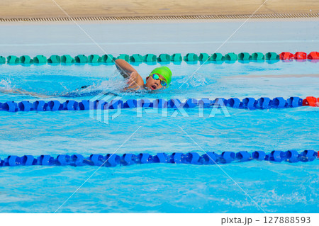 Swimmer child swims freestyle swimming style in a race swimming pool. Water sports and competition, learning to swim classes for children. Swimmer child swims freestyle swimming style in a race swimming pool. Water sports and competition, learning to swim classes for children. 127888593