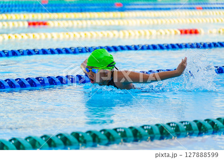 Swimmer child swims butterfly swimming style in a race swimming pool. Water sports and competition, learning to swim classes for children. 127888599