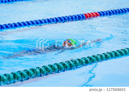 Swimmer child swims backstroke swimming style in a race swimming pool. Water sports and competition, learning to swim classes for children. Swimmer child swims backstroke swimming style in a race swimming pool. Water sports and competition, learning to swim classes for children. 127888601