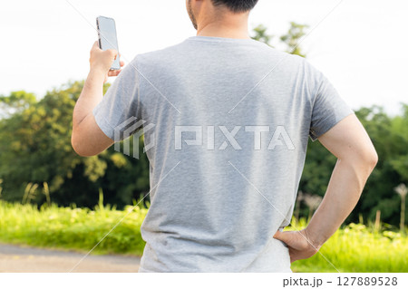 グレーのティーシャツを着た汗だくの中年男性 炎天下でスマホを操作している グレーのティーシャツを着た汗だくの中年男性 炎天下でスマホを操作している 127889528