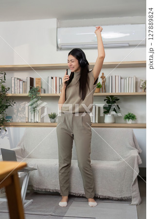 Energetic Dance and Music Enjoyment. Young woman expressing joy while singing at home. Energetic Dance and Music Enjoyment. Young woman expressing joy while singing at home. 127889824