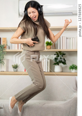 Joyful Music Experience at Home. Young woman dancing and singing with headphones in cozy living room. 127889825