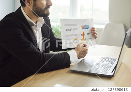Businessman working in office showing finance stat at laptop monitor screen having video call Businessman working in office showing finance stat at laptop monitor screen having video call 127890618