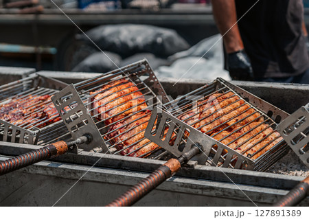 Steaks grilled on iron grill. Grilled meat roasting on open fire in metal baskets at outdoor food stall. Concept of barbecue, street food, smoky flavor Steaks grilled on iron grill. Grilled meat roasting on open fire in metal baskets at outdoor food stall. Concept of barbecue, street food, smoky flavor 127891389
