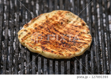 Grilled flatbread cooking over hot coals with golden crust and smoky grill marks. Concept of flatbread preparation and traditional street food flavor 127891393