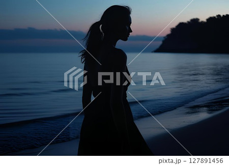 日が暮れた海の浜辺に立つ若い女性のシルエット 127891456